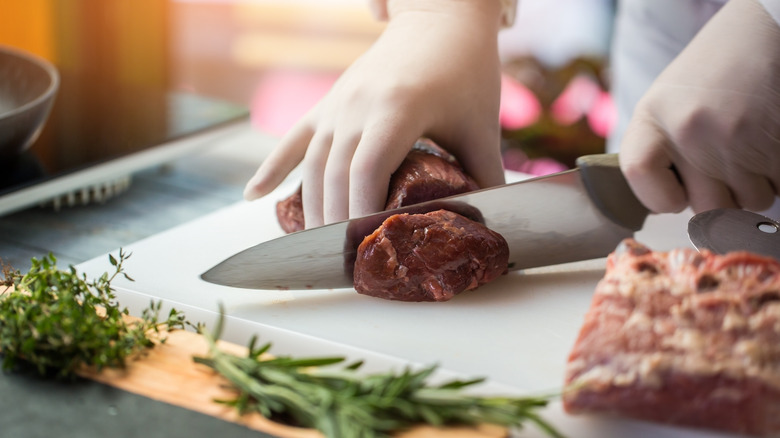 person cutting steak on white cutting board