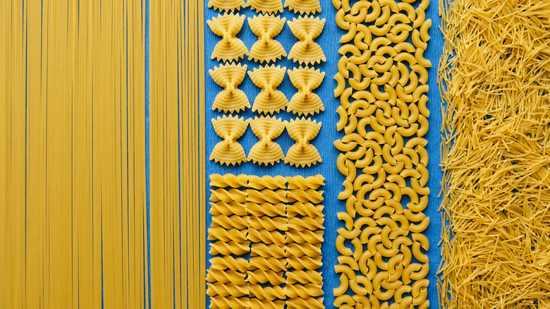 Different types of dry pasta lie on a blue table
