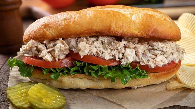 Tuna salad sandwich on hoagie roll with pickles and chips