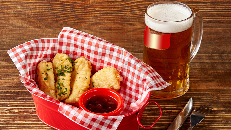 Fried fish in a basket next to clear beer stein