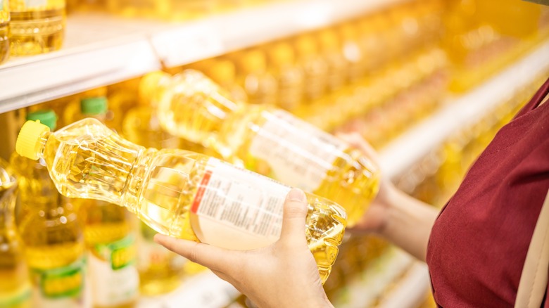 Person choosing bottles of vegetables oils from grocery store shelves