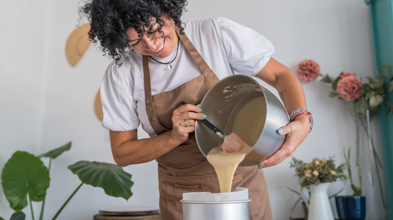 A baker pours cake batter into a cake tin