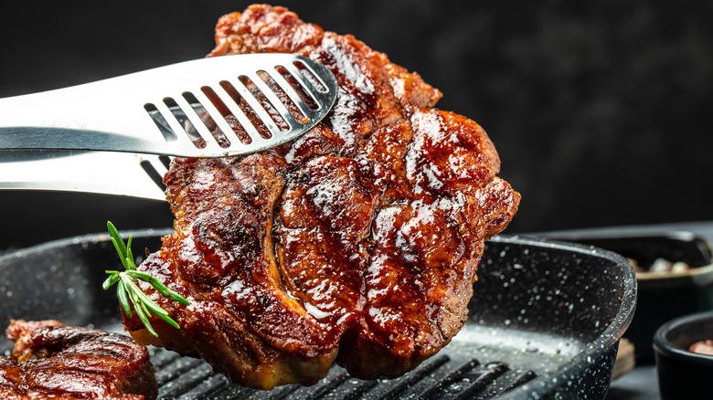 A grilled pork steak held by tongs