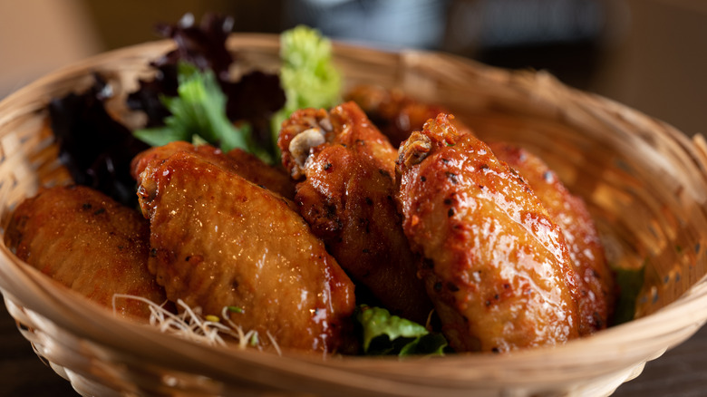 Crispy fried chicken wings in a basket with greens