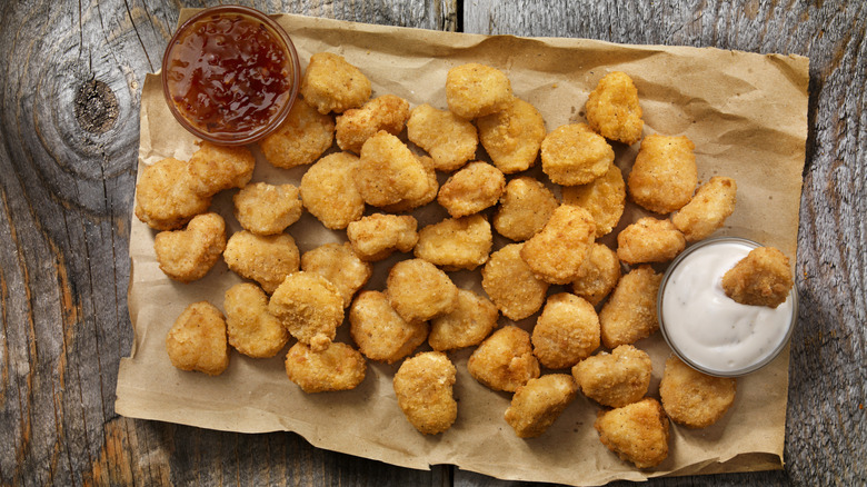 Crispy chicken nuggets on brown paper with dipping sauces.