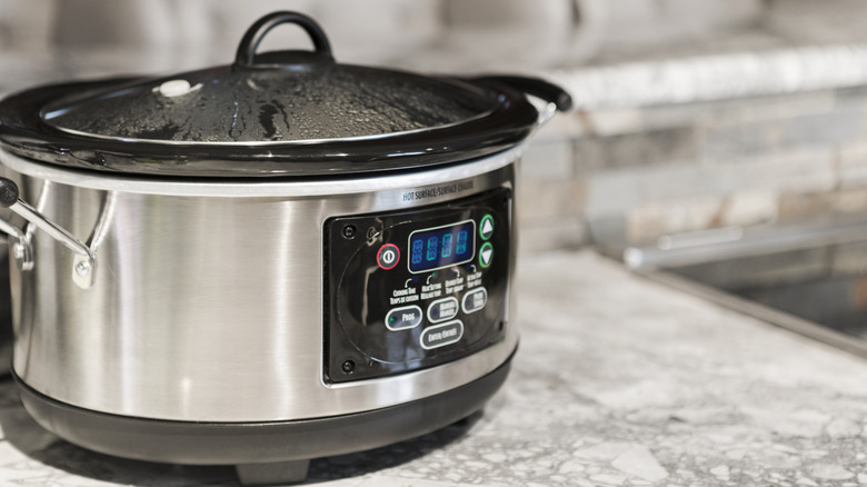 An operating stainless steel slow cooker sits on a kitchen counter