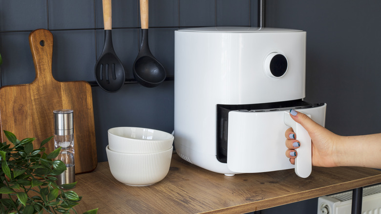 A woman's hand pulls out the basket on a white air fryer