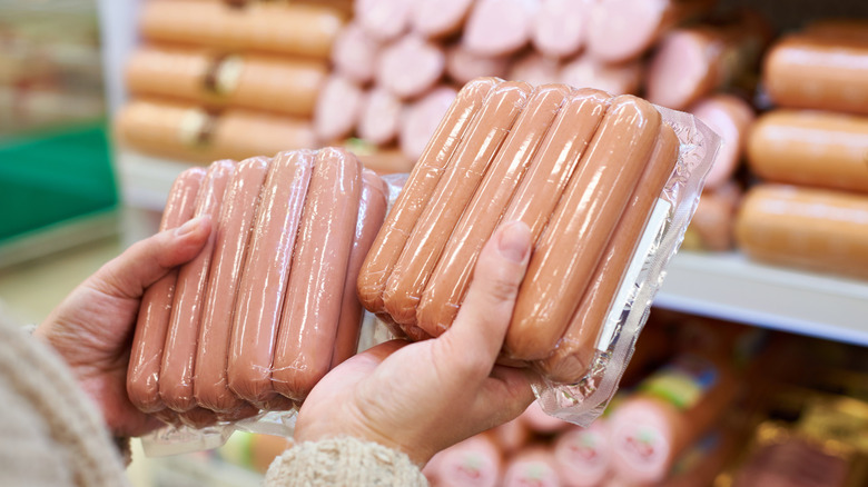 A shopper holds two packs of hot dogs in a supermarket meat aisle