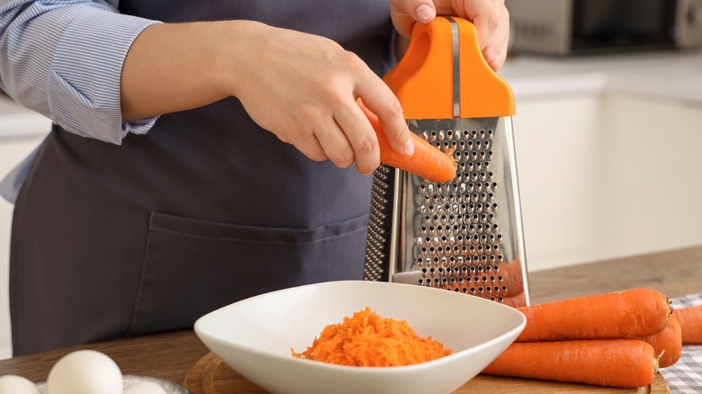 A carrot being grated on a box grater