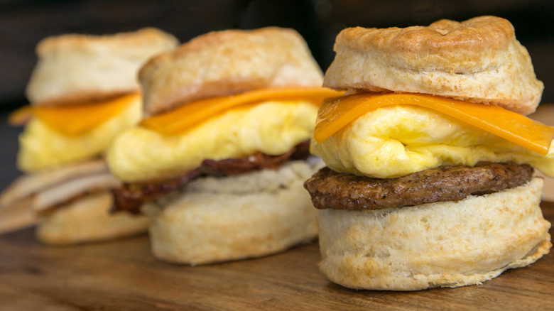 Three sausage, egg, and cheese biscuit sandwiches on wood table