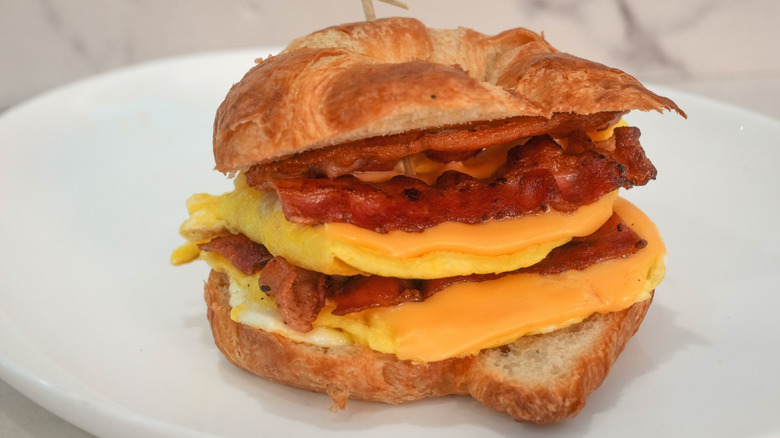 Croissant breakfast sandwich with eggs, cheese, and bacon on white plate