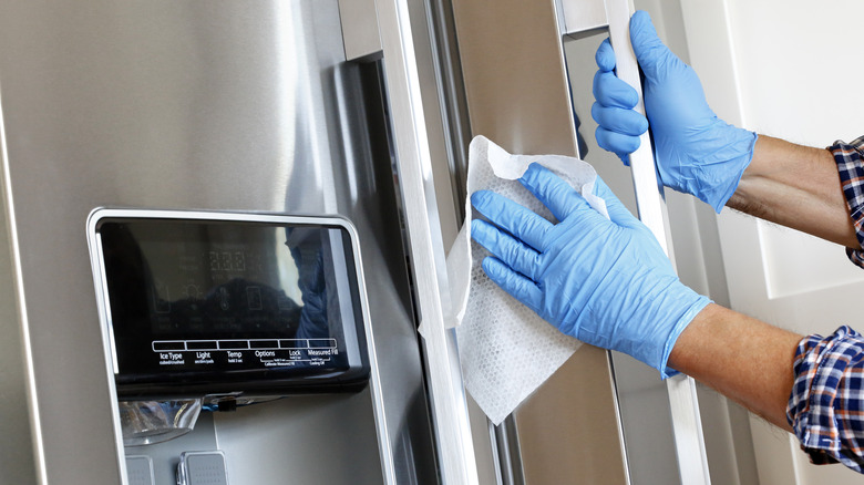 Gloved hands cleaning fridge door