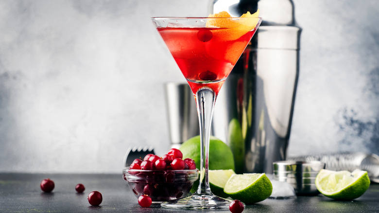 A cosmo surrounded by limes and cranberries.