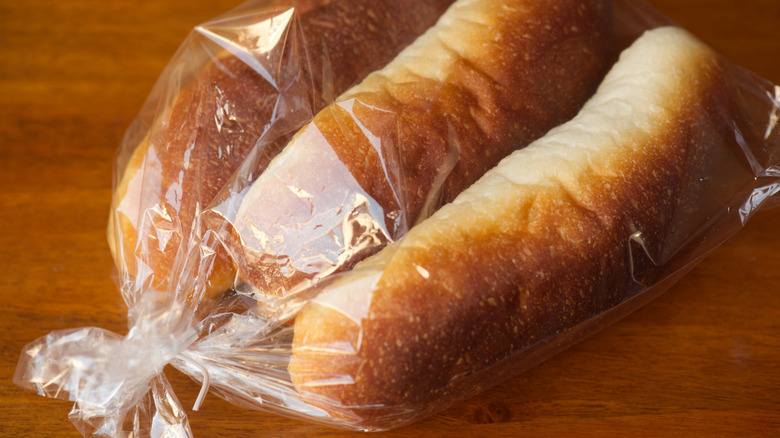 Hot dog buns sit in a clear plastic bag against a dark background