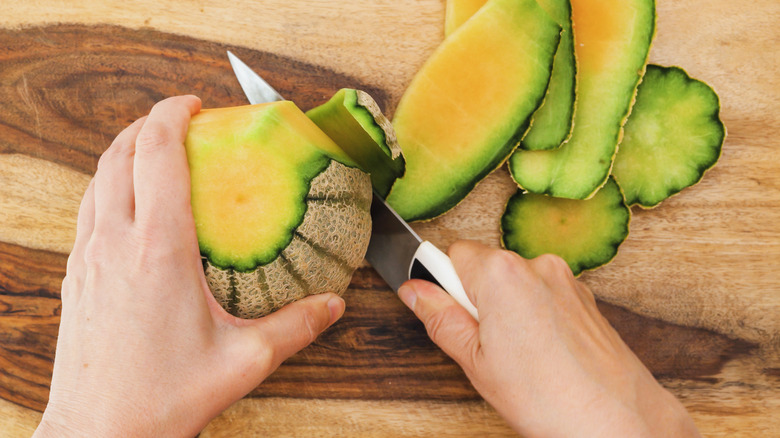 Person peeling whole cantaloupe