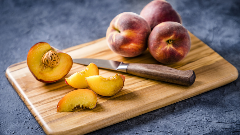 whole and sliced peaches on cutting board with knife