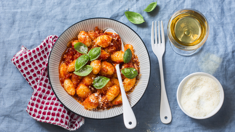 Bowl of gnocchi in tomato sauce next to glass of white wine and cheese