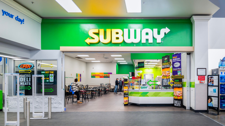 A large Subway logo hangs overhead at the entrance of a Walmart store