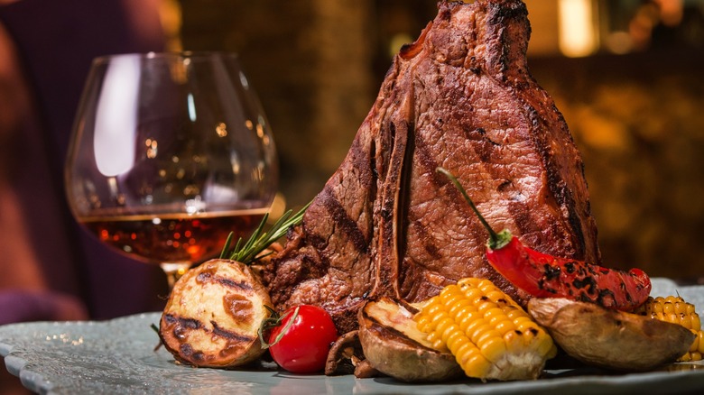 A steak plated attractively with roasted vegetables sits beside a brandy glass