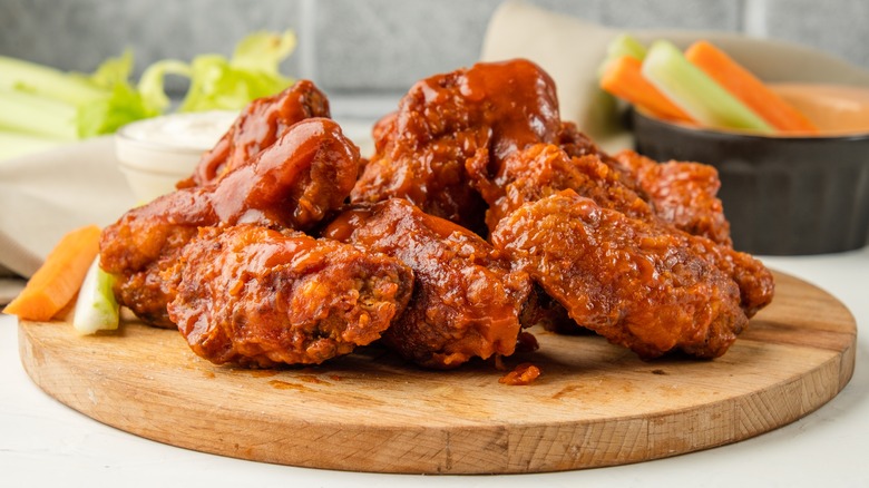 Buffalo chicken wings covered in sauce on round wood cutting board