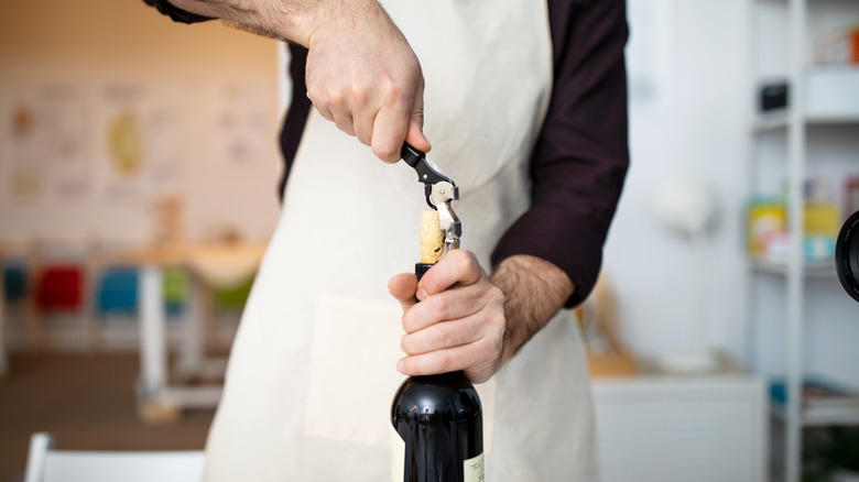 Man in apron uncorking wine bottle