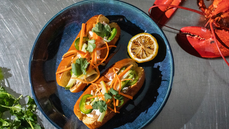 Bahn mi style lobster roll on a blue plate next to a lobster