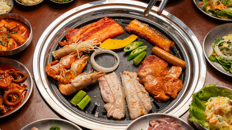 Korean barbecue on a hot plate with tongs surrounded by banchan
