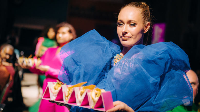 Model in a blue dress holding a tray of tacos