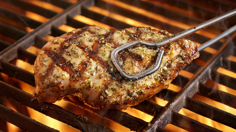 Chicken on the grill being lifted with tongs
