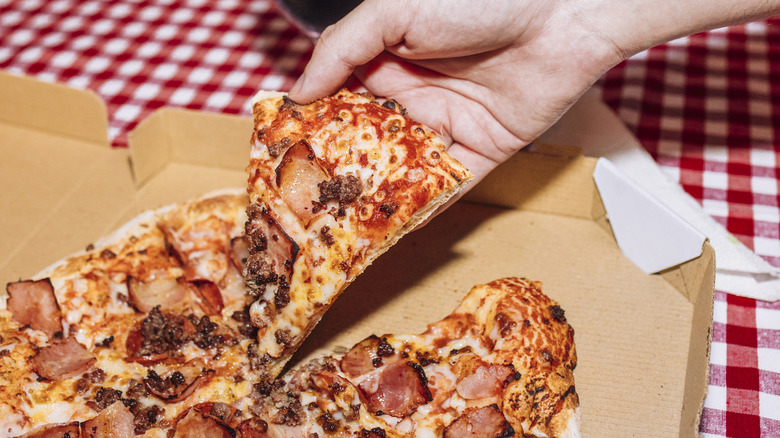 A hand lifts a slice of pizza from a box