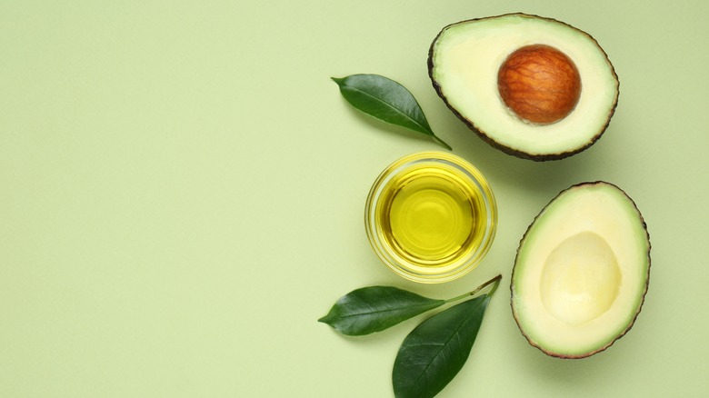 Sliced avocado, leaves, and avocado oil on green background