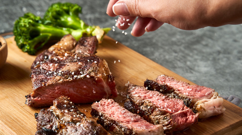 A hand sprinkling salt over a cooked steak