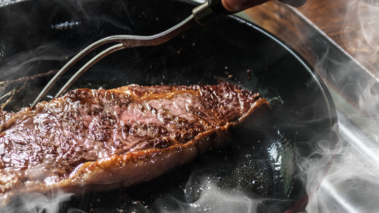 A hand poking a steak with a fork while it's in the skillet
