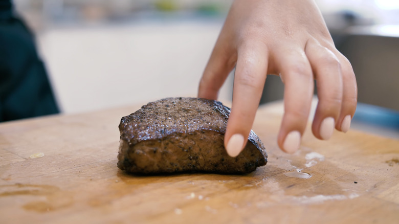 A hand checks the doneness of a steak