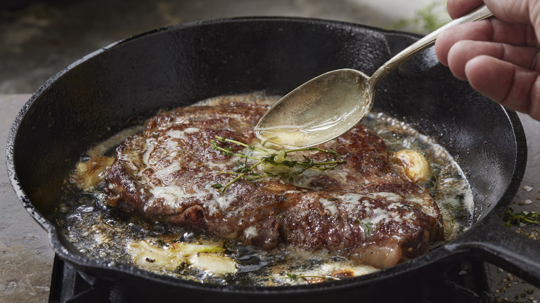 A hand basting a steak in a pan