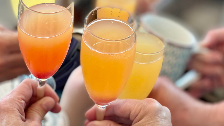 Hands holding various glasses of mimosa