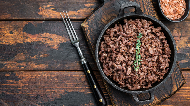 A small cast iron skillet has cooked ground beef in it.