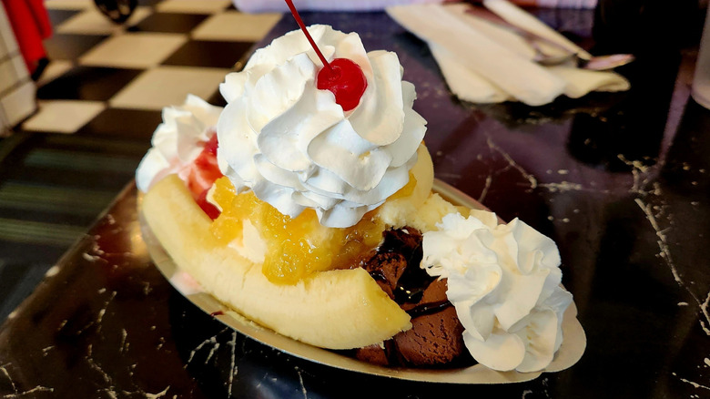 A sundae, featuring House of Flavors ice cream, sits in a metal bowl on a black table