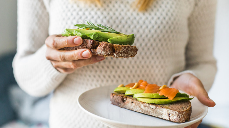 Someone holds an open-faced sandwich with avocado and salmon.
