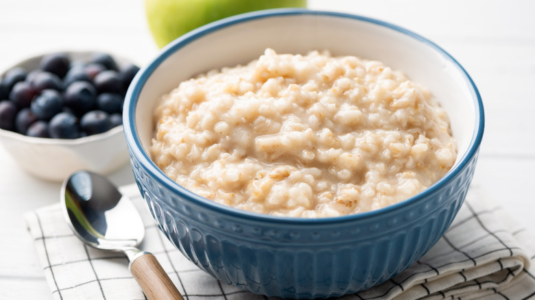Breakfast setting with plain cooked oatmeal in blue bowl with spoon
