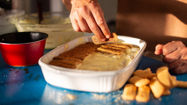 Person making tiramisu with ladyfingers in white dish