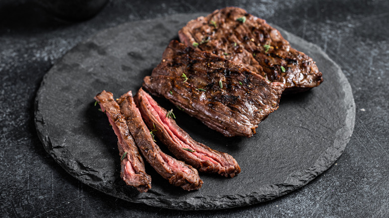 A skirt steak, partially sliced, on a black stone dish.