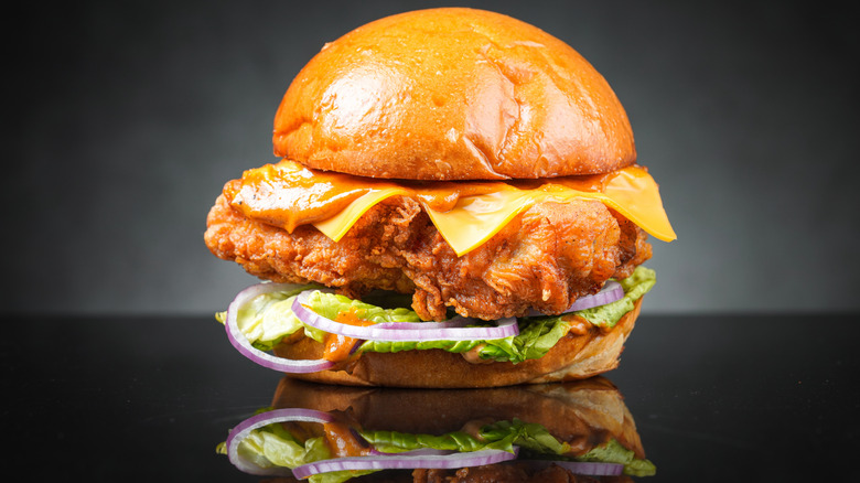 A spicy chicken sandwich with sauce, cheese, red onions, and lettuce against a dark background