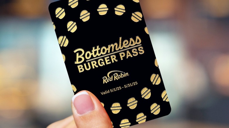 A close up of a female hand holding a black and gold Red Robin card reading "Bottomless Burger Pass"