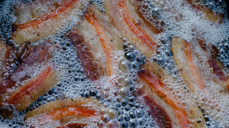 Bacon frying in a pan, surrounded by bacon grease