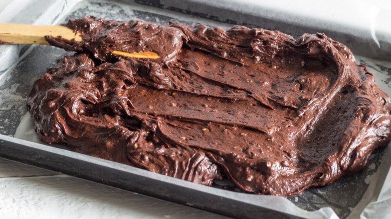 Brownie batter is spread into a baking pan with a wooden spoon