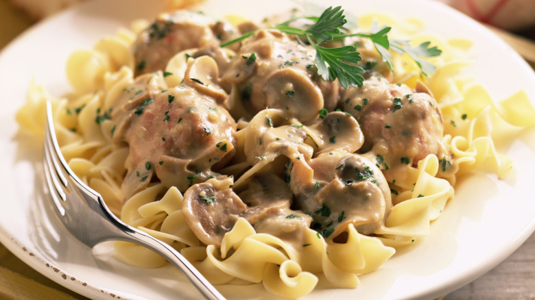 Beef stroganoff served over noodles on a white plate