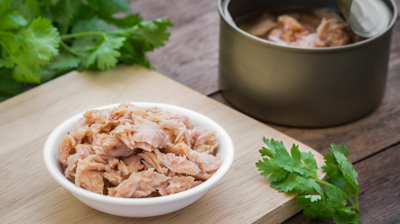 Open can of tuna next to a bowl of tuna