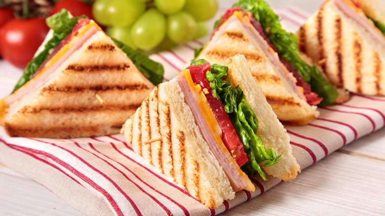 Four sandwich halves cut into triangle shapes, filled with ham, cheese, tomato, and lettuce