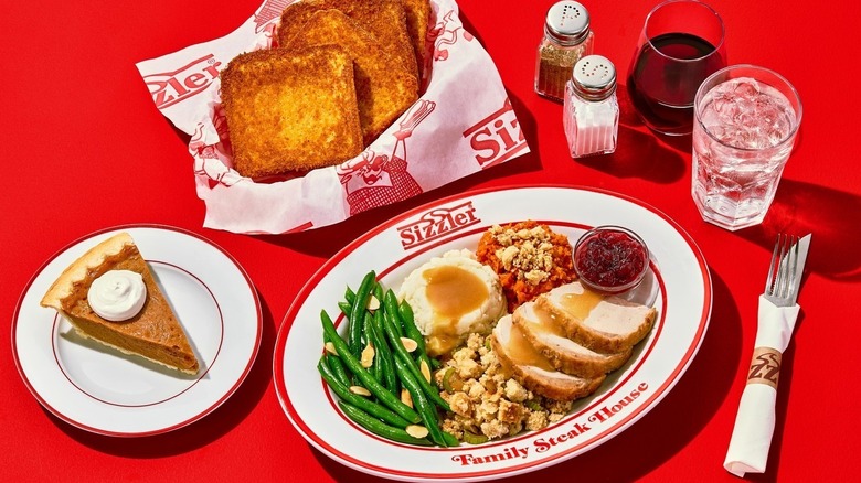 Various plates of food from Sizzler steak house on red background